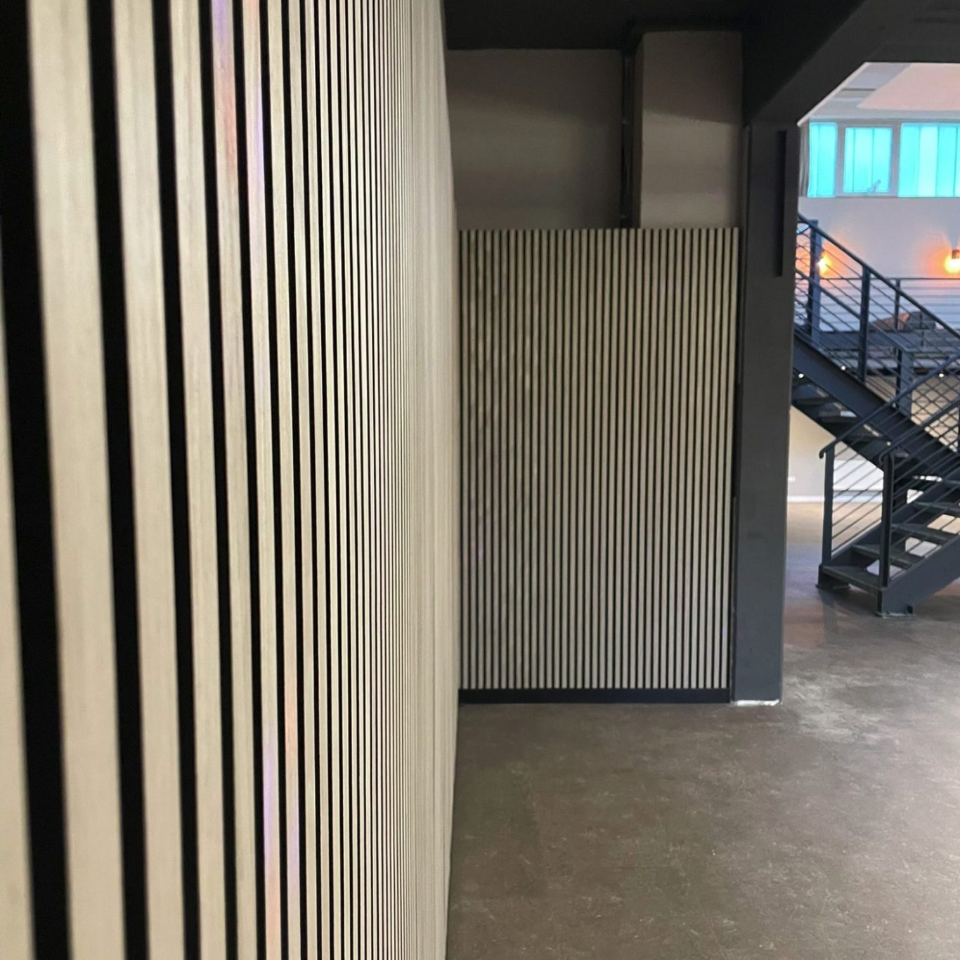 Holzlattenwand in modernem Innenraum, im Hintergrund eine Treppe.