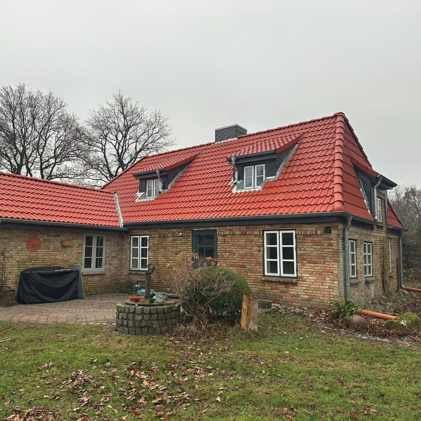 Steinbauernhaus mit rotem Dach, umgeben von Bäumen und einer Wiese.