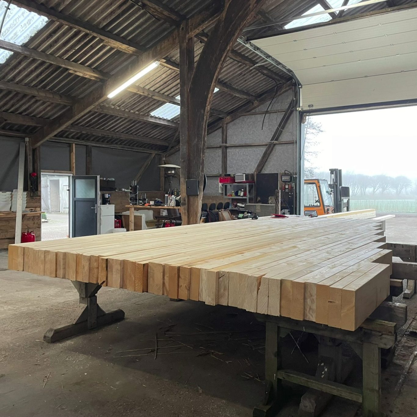 Eine große Holzplatte liegt auf einem Tisch in einer Werkstatt mit weiteren Holzstücken.