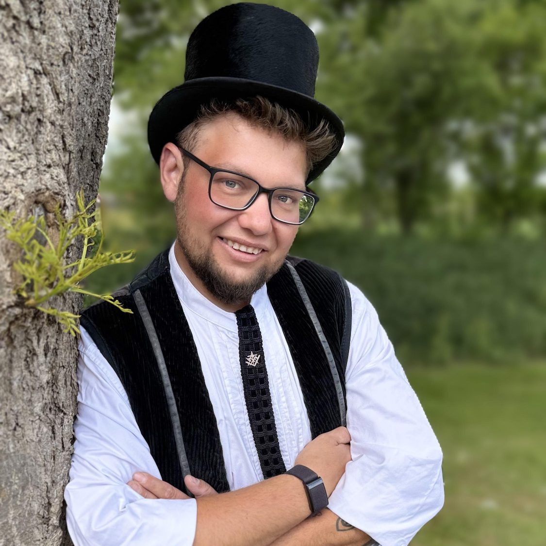 Junger Mann in Zylinder und klassischer Kleidung steht an einem Baum.