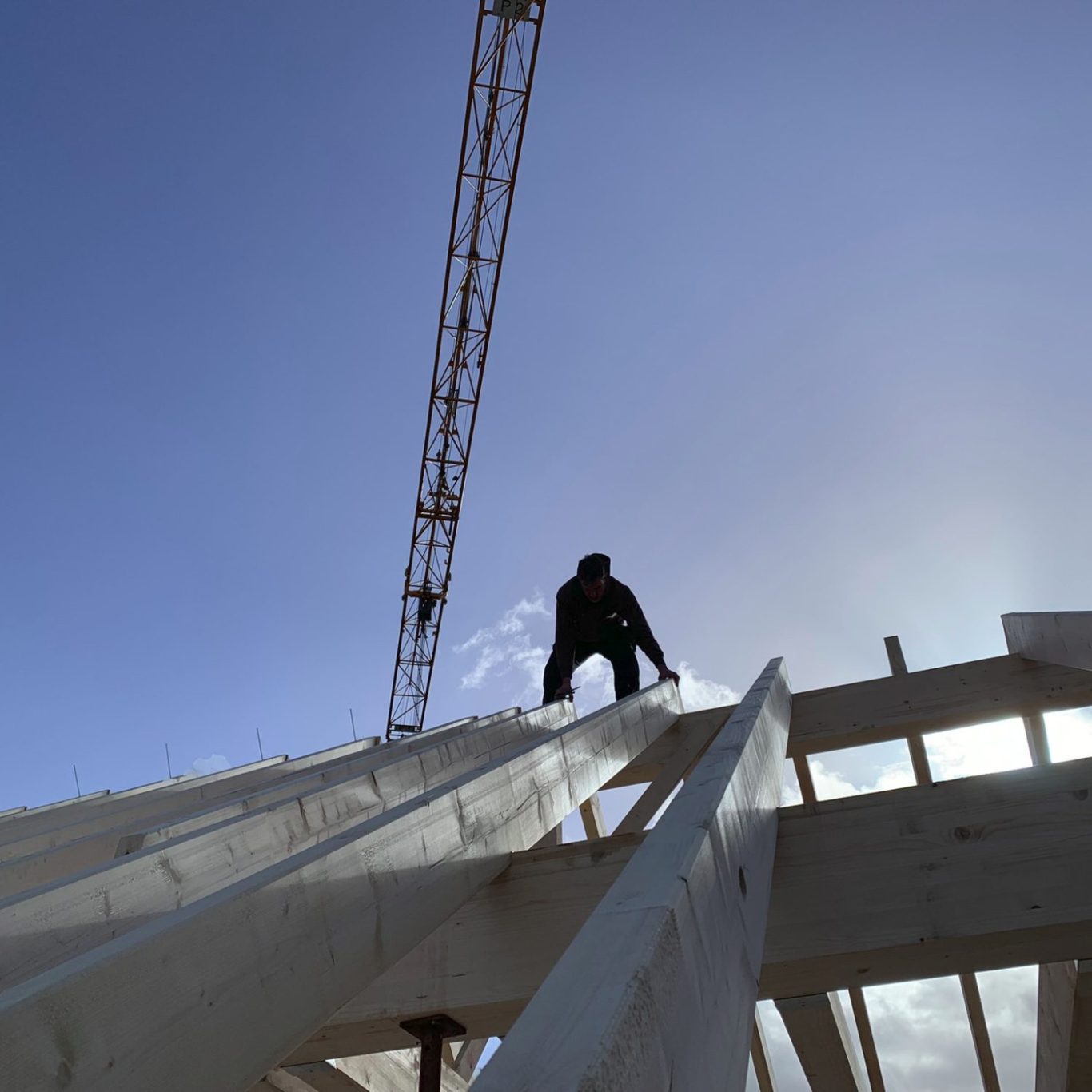 Arbeiter auf einem Baugerüst unter einem klaren Himmel, mit einem Kran im Hintergrund.
